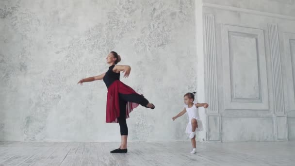egy kis vicces lány megpróbálja megismételni a mozgás mögött a balerina a balett osztályban. lassú mozgás - Felvétel, videó