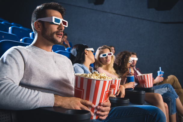 selective focus of multiethnic friends in 3d glasses with popcorn watching film together in movie theater - Photo, Image