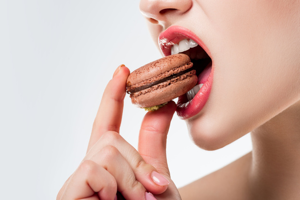 cropped view of woman biting chocolate french macaroon, isolated on white - Photo, Image