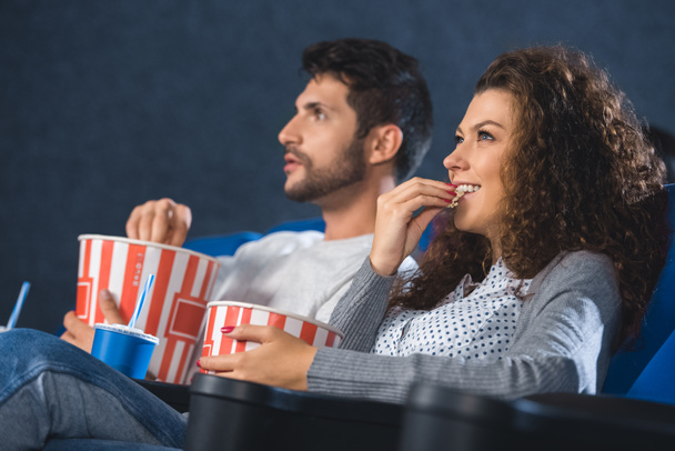 couple eating popcorn while watching film together in cinema - Foto, Imagem