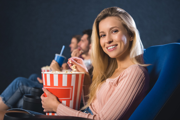 selective focus of smiling woman with popcorn in cinema - Foto, afbeelding