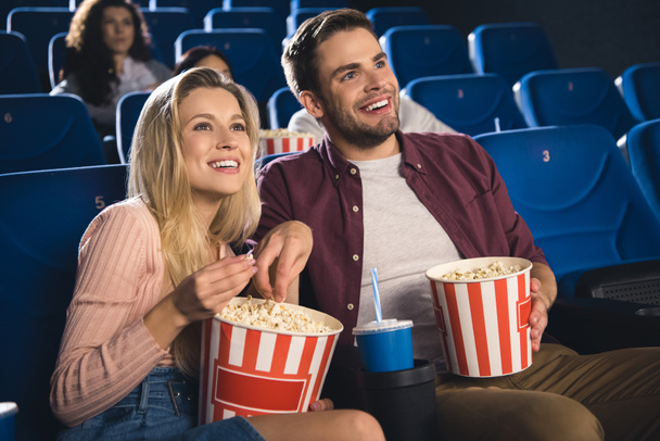 smiling couple with popcorn and soda drink watching film together in cinema - Photo, Image