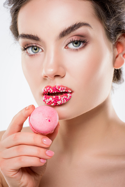 attractive woman with sugar sprinkles on lips holding pink macaron, isolated on white - Photo, Image
