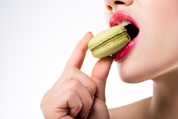 abgeschnittene Ansicht einer Frau, die in grünen Macaron beißt, isoliert auf weiß - Foto, Bild