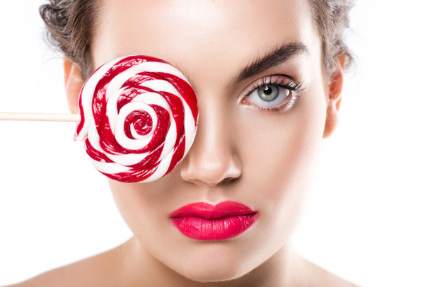 attractive young woman holding red lollipop in front of eye, isolated on white - Zdjęcie, obraz