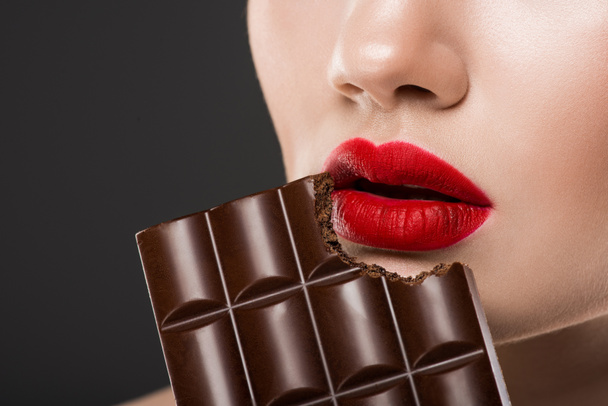 グレーに分離、チョコレート ・ バーを食べる真っ赤な唇を持つ女性のトリミング ビュー - 写真・画像