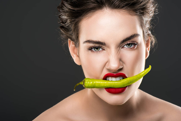 sexy woman holding green chili pepper in teeth, isolated on grey - Фото, изображение