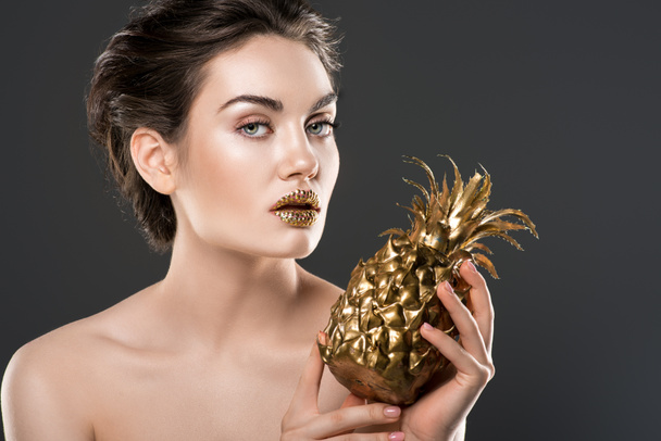 attractive naked woman with golden makeup holding pineapple, isolated on grey - Foto, Imagem