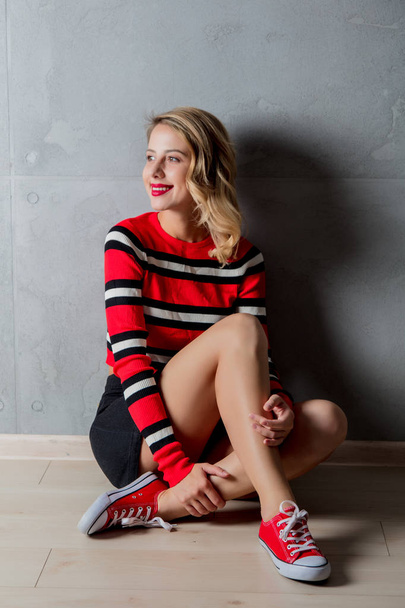 young stylish blonde woman in red striped sweater posing on grey background - Фото, изображение