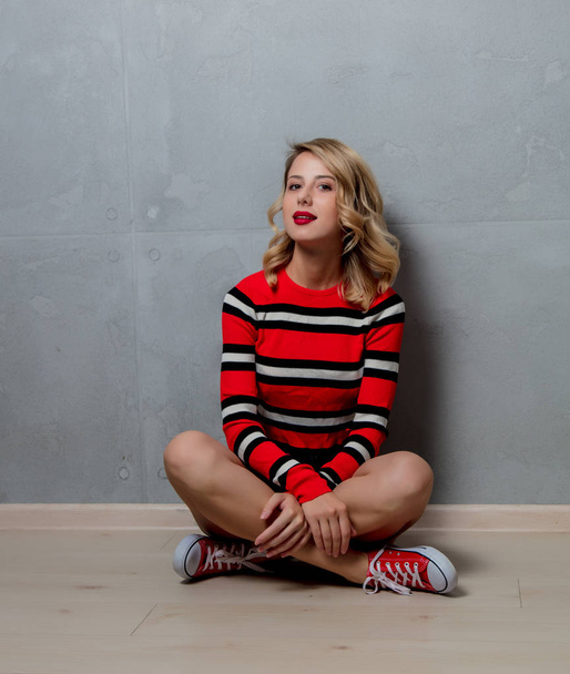 молодая стильная блондинка в красно-полосатом свитере позирует на сером фоне
 - Фото, изображение