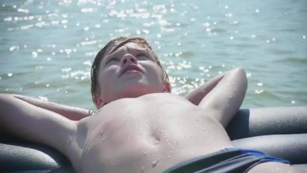 Ένας νεαρός άντρας είναι το κολύμπι στη θάλασσα σε ένα φουσκωτό στρώμα. Θετικά συναισθήματα. Ζεστή μέρα του καλοκαιριού - Πλάνα, βίντεο