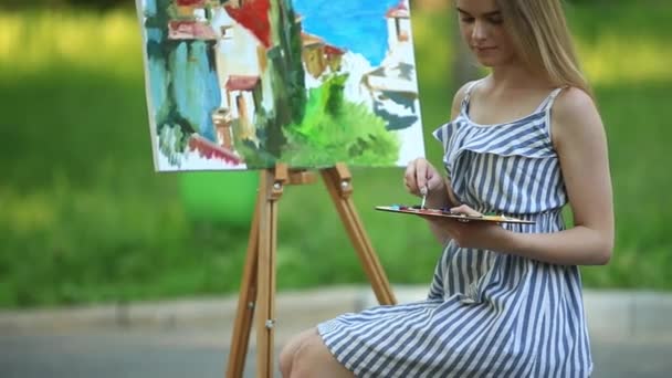 Krásná dívka umělec je na stoličce v parku a hospodářství paleta s barvami - Záběry, video