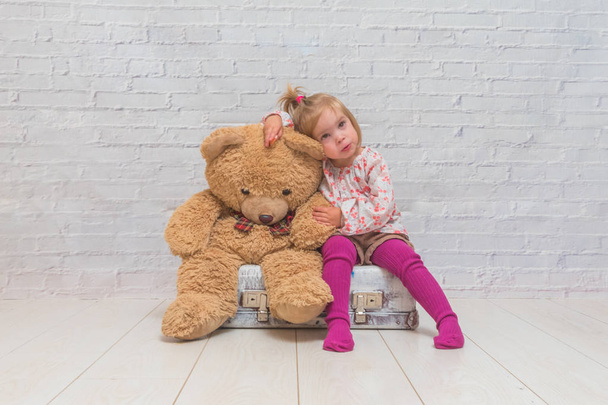 girl, child with bear and suitcase on white brick wall background - Foto, imagen