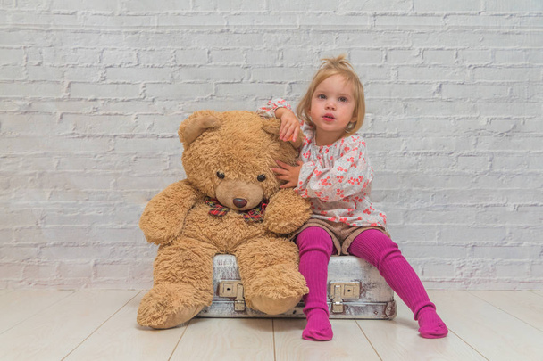 girl, child with bear and suitcase on white brick wall background - Foto, afbeelding