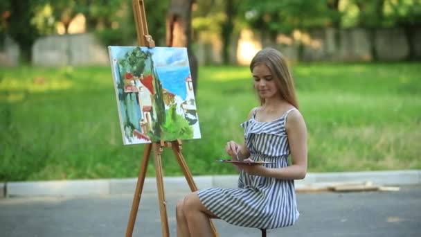 Gyönyörű lány művész a széken, a park és a gazdaság palettán, a festékek - Felvétel, videó