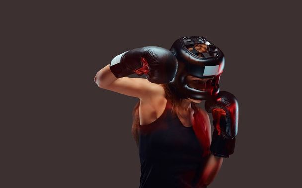 Retrato de una boxeadora con casco protector y guantes durante los ejercicios de boxeo, enfocado en un proceso con rostro concentrado serio
. - Foto, Imagen