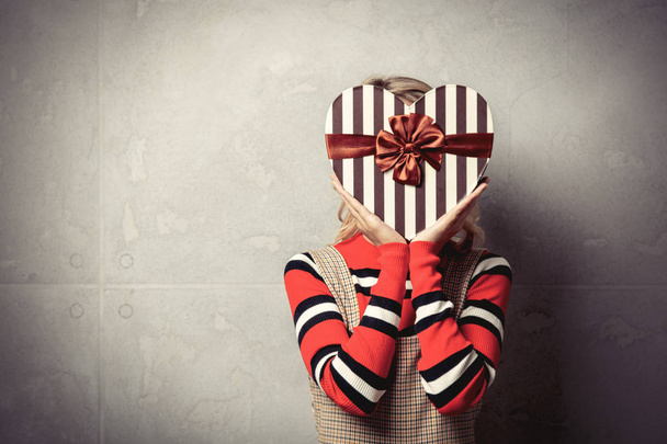 Young girl with heart shape gift box on grey background - Fotoğraf, Görsel
