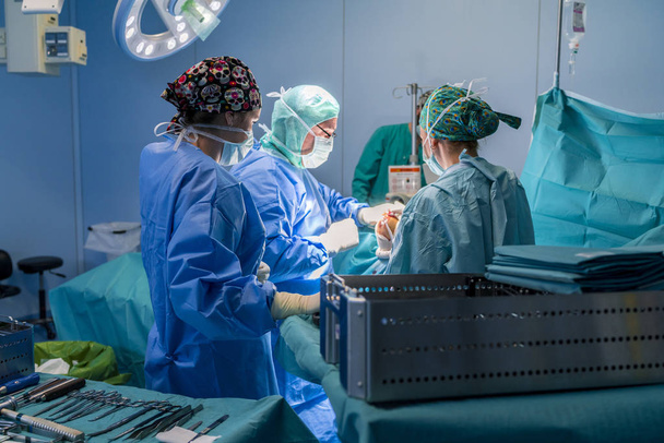 Chirurg, chirurgisch assistent en verpleegkundige werken in de operatiekamer ziet het chirurgisch materiaal. Ze worden verlicht door het licht van de operatiekamer. - Foto, afbeelding
