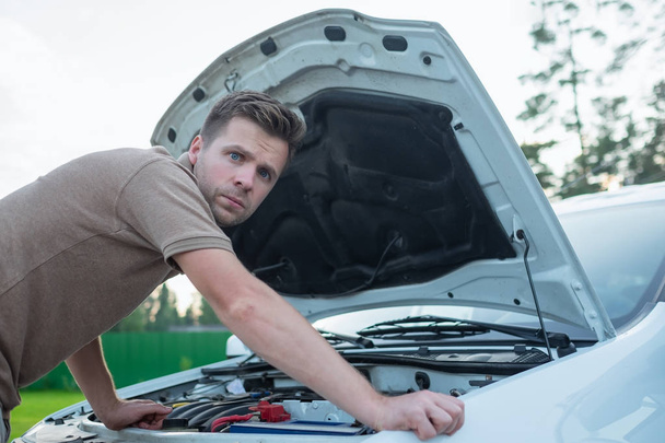 young stressed man having trouble with his broken car looking in frustration at failed engine - 写真・画像