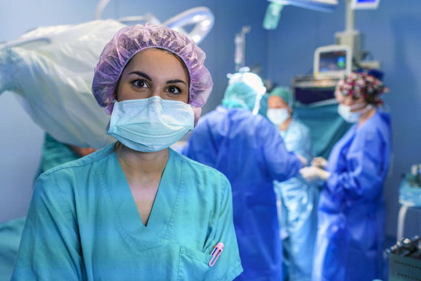 Chirurgia asystent patrząc na kamery z zespołu chirurgii, działa w tle. Ma na sobie fioletowy kapelusz. - Zdjęcie, obraz