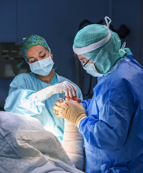 Chirurg, asystent chirurgiczny i pielęgniarka pracuje w sali operacyjnej można zobaczyć materiały chirurgiczne. Są one oświetlone przez światło sali operacyjnej. - Zdjęcie, obraz