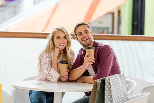  happy couple with shopping bugs at table with disposable cups of coffee in cafe  - Foto, imagen