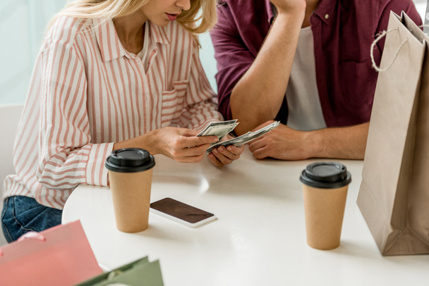 partial view of young couple counting cash money at table with coffee cups in cafe  - Photo, Image