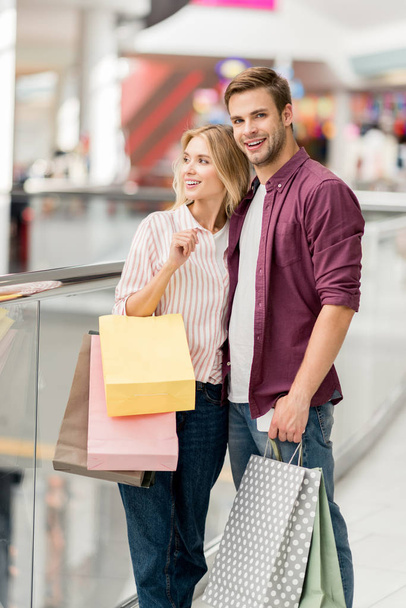 молода усміхнена пара з сумками для покупок та смартфона в торговому центрі
  - Фото, зображення