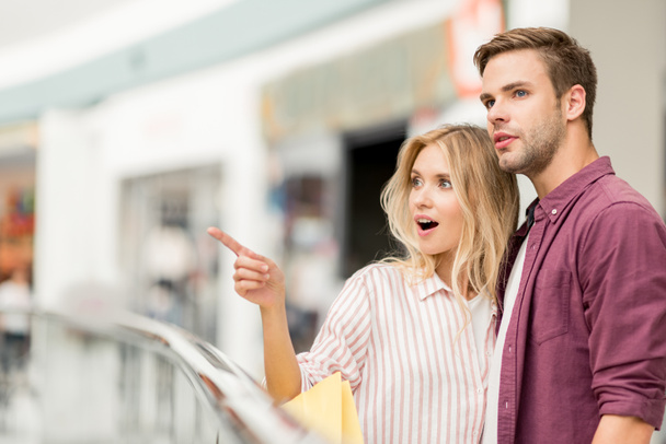 selective focus of young woman with shopping bags pointing to boyfriend at shopping mall - Foto, Imagen