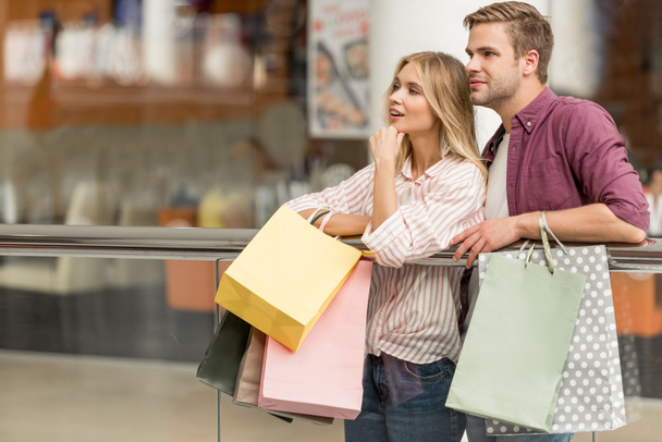 sorrindo casal de compradores com sacos de papel em pé no shopping
  - Foto, Imagem