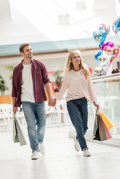 happy young couple of shoppers with paper bags walking at shopping mall  - Fotografie, Obrázek