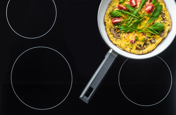 top view of omelette in frying pan cooking on black stove - Foto, Imagem