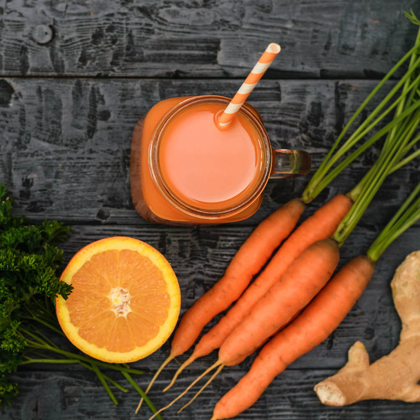 A mug filled with fresh carrot smoothie and a bunch of carrots on a wooden table. The view from the top. The concept of healthy eating. Flat lay. - Fotoğraf, Görsel