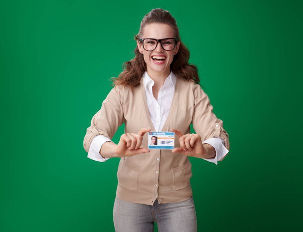 happy young student woman showing student card on green background - Foto, imagen