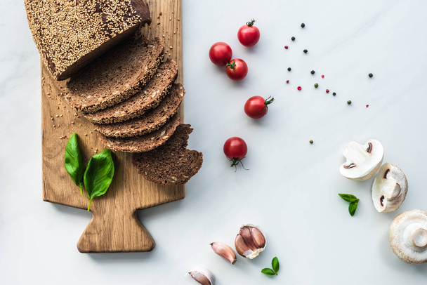 tasainen lay kanssa leikattu leipä puinen leikkuulauta, mustapippuri ja vihannekset ruoanlaittoon aamiainen valkoinen marmori pinnalla
 - Valokuva, kuva