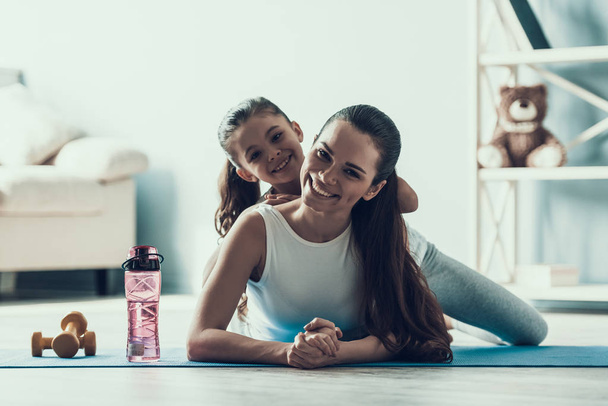 Young Woman and Little Girl Resting after Exercise. Beautiful Young Mother and Adorable Little Daughter Lying on Yoga mat. Mother and Daughter Together at Home. Healthy Lifestyle - Zdjęcie, obraz