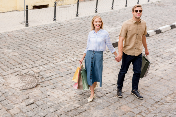 magas, szög, kilátás a stílusos vásárlók papír táskák: város utca sétáló pár - Fotó, kép