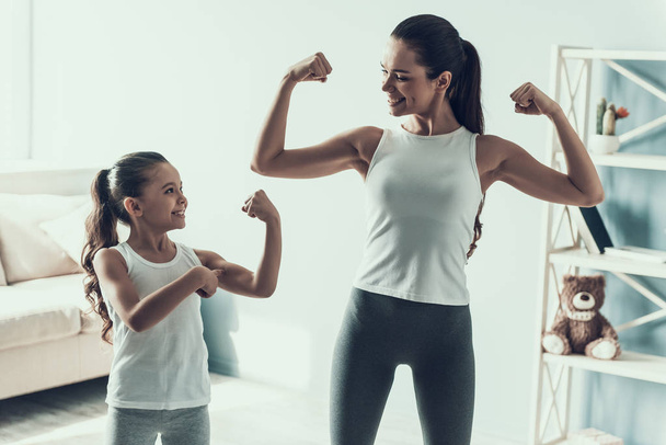 Young Woman and Little Girl doing Fitness Exercise. Beautiful Young Mother and Adorable Little Daughter during Exercise. Mother and Daughter showing Muscles Together at Home. Healthy Lifestyle - Photo, Image