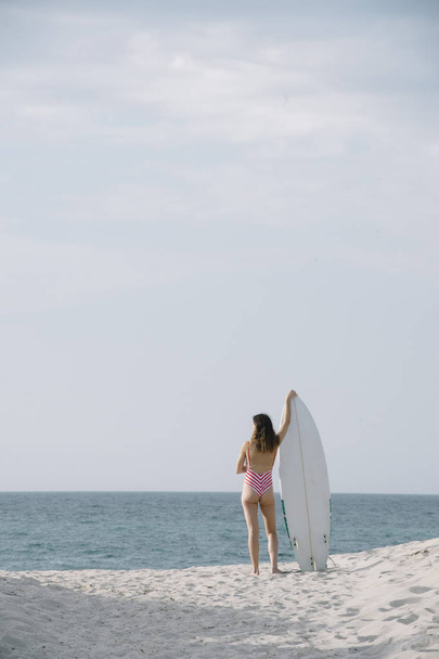 Retrato de uma surfista em uma praia segurando uma prancha
 - Foto, Imagem