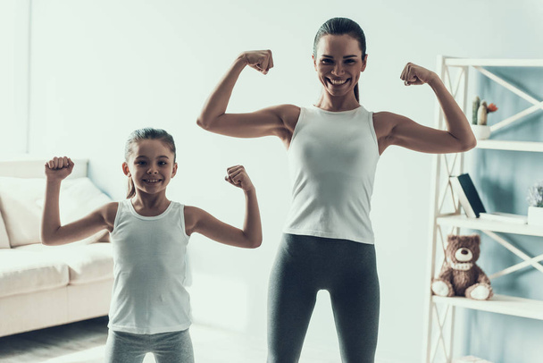 Young Woman and Little Girl doing Fitness Exercise. Beautiful Young Mother and Adorable Little Daughter during Exercise. Mother and Daughter showing Muscles Together at Home. Healthy Lifestyle - Фото, зображення