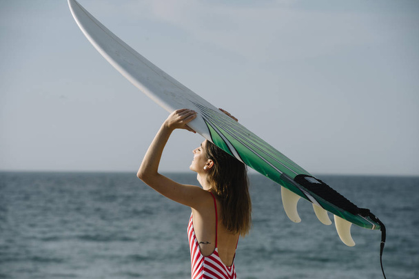 Sörf tahtası tutan bir plajda bir sörfçü kadın portresi - Fotoğraf, Görsel