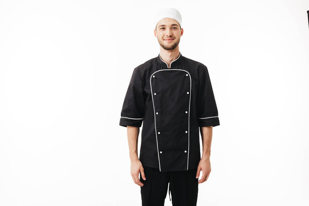 Giovane chef in uniforme nera e cappuccio bianco sognante guardando in macchina fotografica su sfondo bianco
 - Foto, immagini