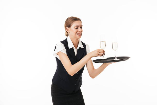 junge Kellnerin in Uniform versucht Tablett mit Gläsern über weißem Hintergrund isoliert zu halten - Foto, Bild