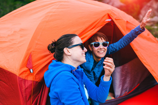 Two girls are sitting in a tent. Girlfriends communicate in nature. Women in sleeping bags drink coffee. Friends in the campsite. Smiling brunettes talking. - Photo, Image