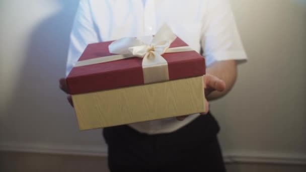 ein junger Mann streckt sich und schenkt eine Schachtel mit einem Geschenk - Filmmaterial, Video