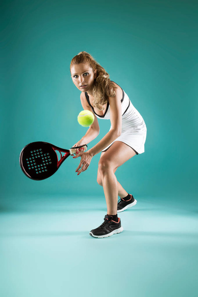 Shot of pretty young woman playing padel indoor over green-blue background. - Foto, immagini