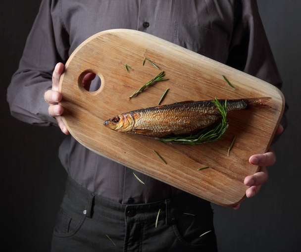 Man with smoked herring on a dark background.  - Photo, Image