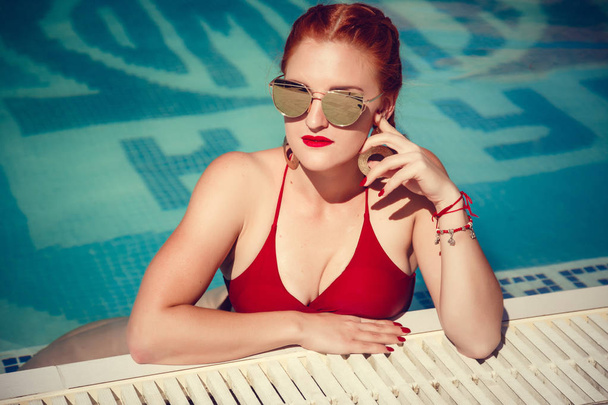 Απολαμβάνοντας ηλιοθεραπεία και διακοπές. Πολύχρωμο πορτρέτο του όμορφη νεαρή γυναίκα με κόκκινο μαγιό που βρίσκεται κοντά στην πισίνα. - Φωτογραφία, εικόνα