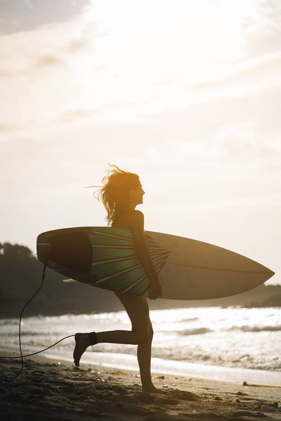 Woman with surfboard standing on wet sandy beach at the ocean. - Fotó, kép