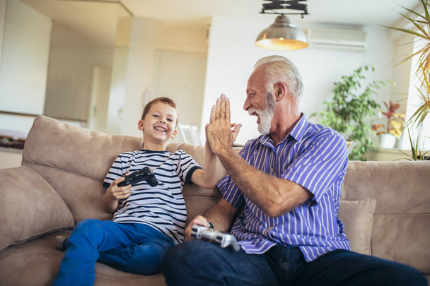 Παππούς και εγγονός παίζουν βιντεοπαιχνίδια στο σπίτι. - Φωτογραφία, εικόνα
